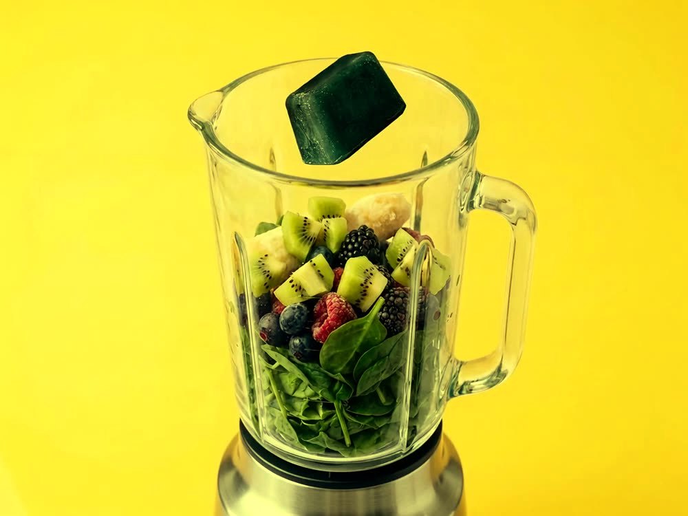 A SimpliiGood spirulina cube dropping into a blender, blending and pouring out as a green smoothie